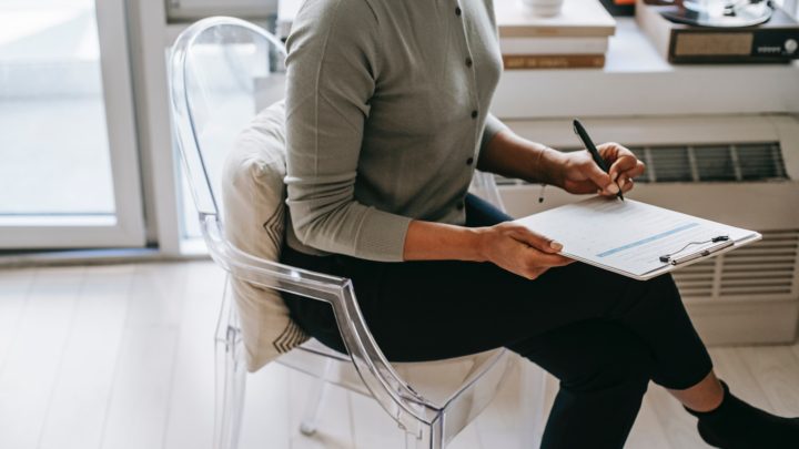 Image of a woman sitting at a desk, filling out a paper form with a pen.